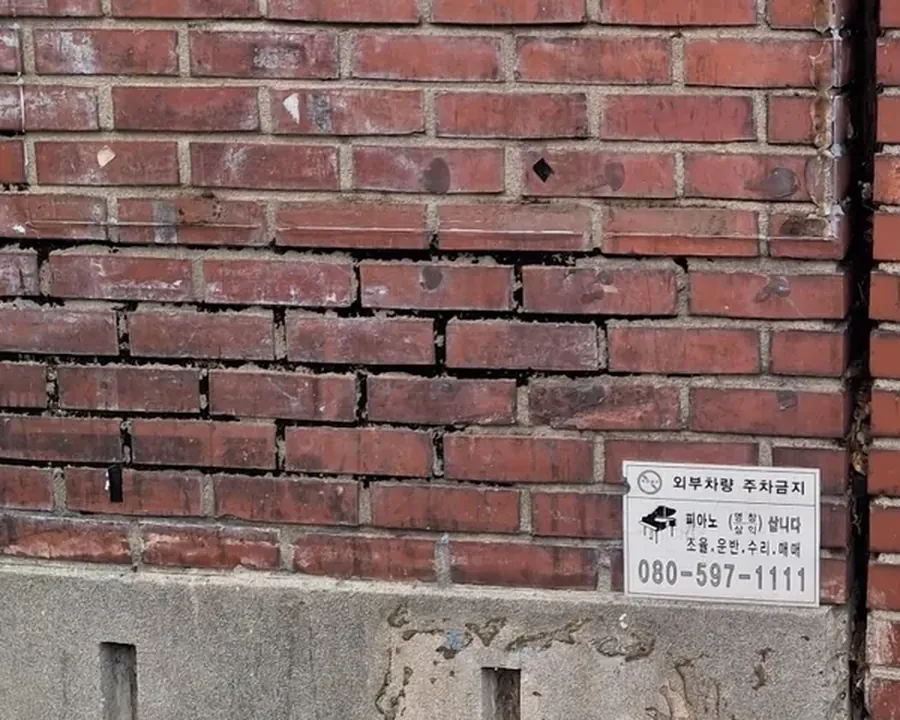 벽돌 담장 하부 줄눈이 수평으로 벌어지고 일부 벽돌이 움직인 상태