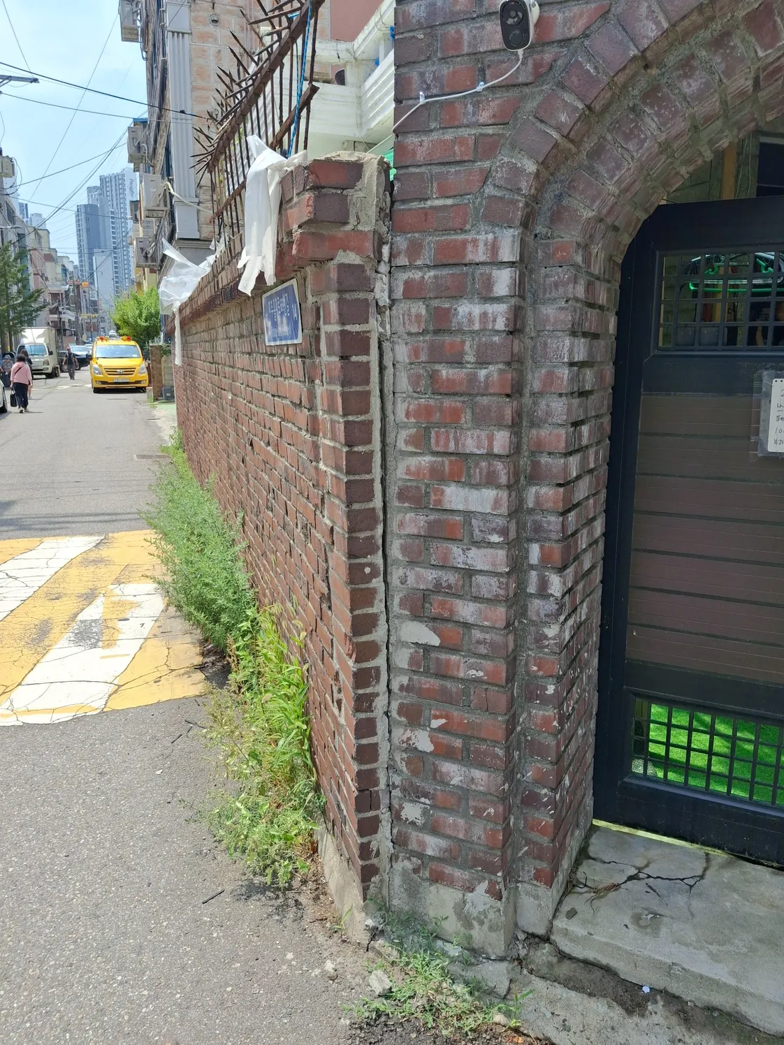 담벼락무너짐보수 전 대문 기둥과 벽돌 담장 사이가 벌어지고 위쪽 벽돌이 빠진 모습