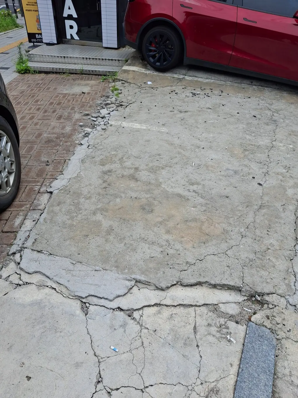 주차장 진입로 콘크리트 가장자리가 깨져 파편이 떨어지고 긴 균열이 이어진 작업 전 상태